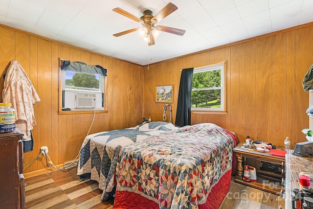 bedroom featuring hardwood / wood-style flooring, wood walls, cooling unit, and ceiling fan