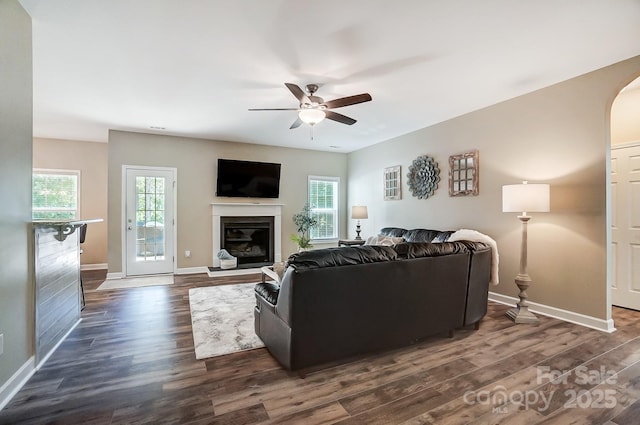 living room with baseboards, arched walkways, dark wood finished floors, and a glass covered fireplace