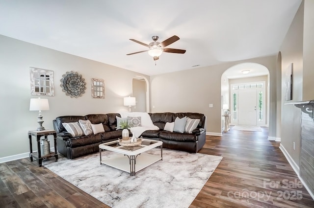 living area featuring arched walkways, baseboards, and wood finished floors