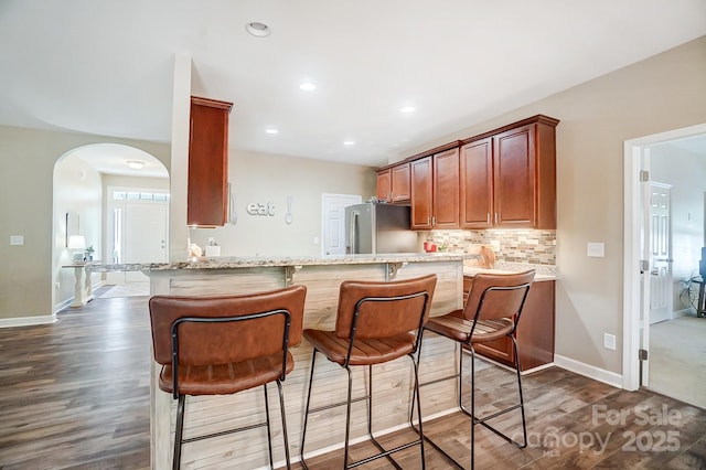 kitchen featuring arched walkways, dark wood-type flooring, backsplash, and freestanding refrigerator