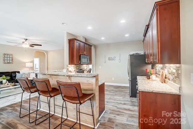 kitchen with arched walkways, stainless steel appliances, a peninsula, open floor plan, and a kitchen bar