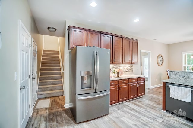 kitchen featuring appliances with stainless steel finishes, light wood-type flooring, light stone counters, and decorative backsplash