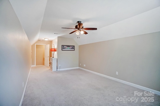 empty room featuring lofted ceiling, light colored carpet, visible vents, ceiling fan, and baseboards