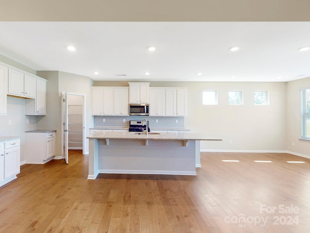 kitchen featuring stainless steel appliances, light hardwood / wood-style floors, white cabinetry, and a kitchen island with sink