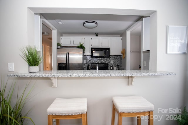 kitchen featuring stainless steel fridge, decorative backsplash, a kitchen bar, and white cabinets