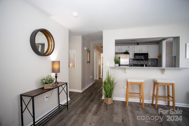 kitchen featuring tasteful backsplash, white cabinets, stainless steel fridge, a breakfast bar, and dark hardwood / wood-style floors