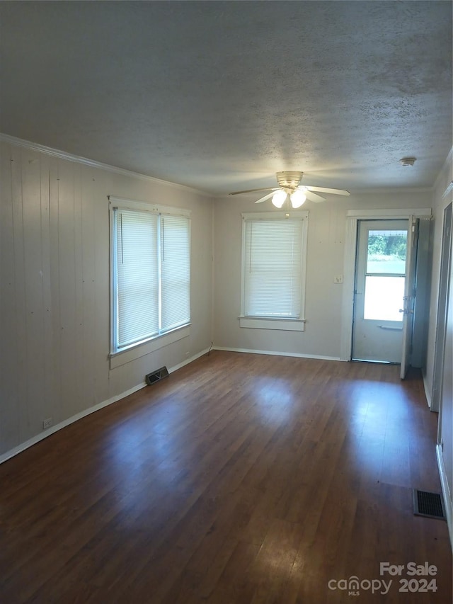 empty room with ceiling fan, ornamental molding, dark wood-type flooring, and a textured ceiling