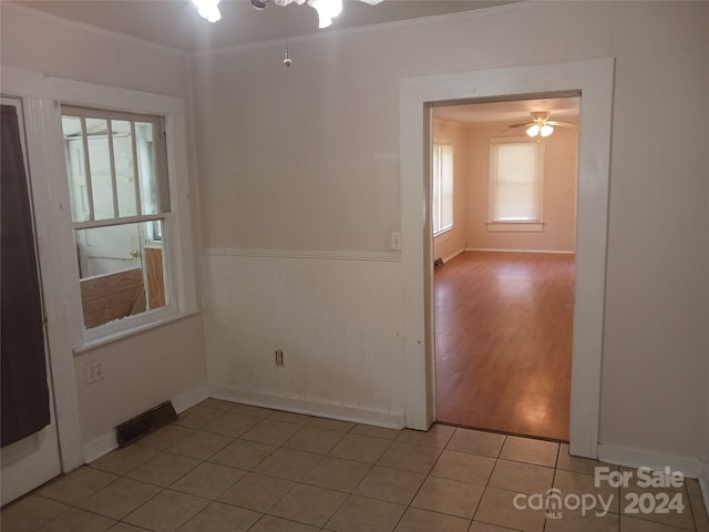 empty room with light tile patterned flooring, ornamental molding, a wealth of natural light, and ceiling fan