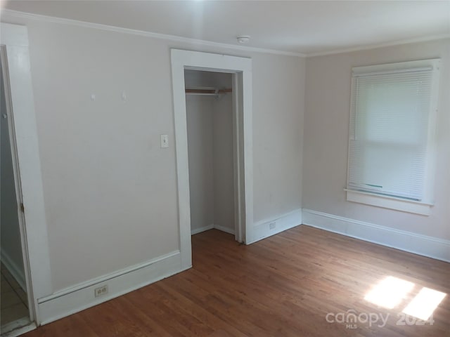 unfurnished bedroom with dark wood-type flooring, ornamental molding, and a closet