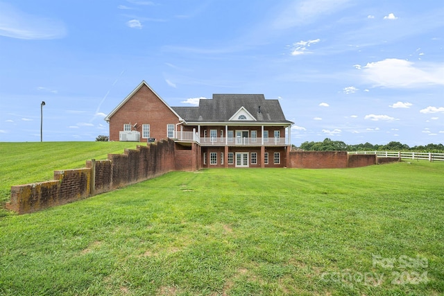 back of house featuring a balcony, fence, a lawn, and brick siding