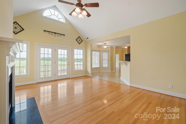 unfurnished living room with light wood finished floors, baseboards, ceiling fan, high vaulted ceiling, and a high end fireplace