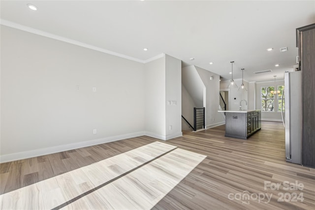 unfurnished living room with sink, ornamental molding, a notable chandelier, and light wood-type flooring