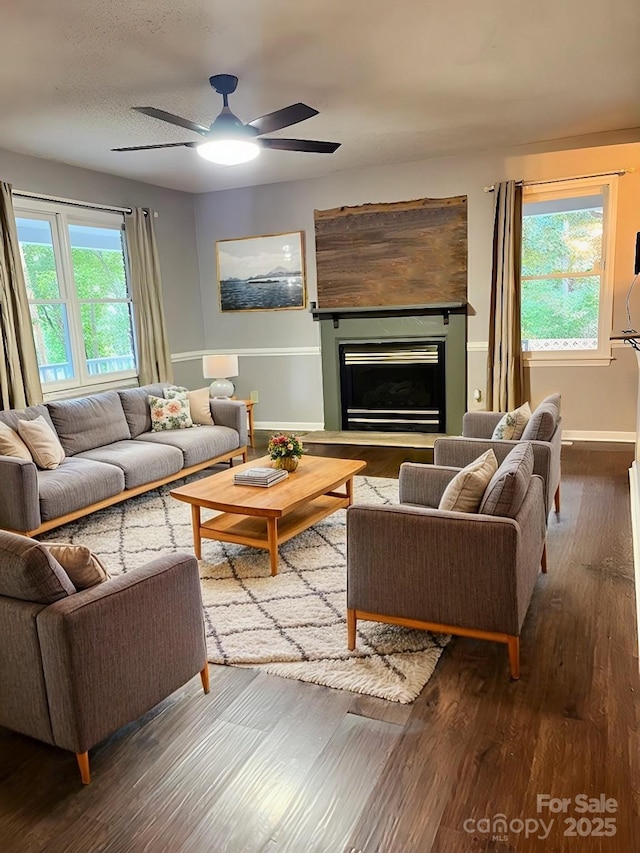 living area with a ceiling fan, a glass covered fireplace, a textured ceiling, wood finished floors, and baseboards