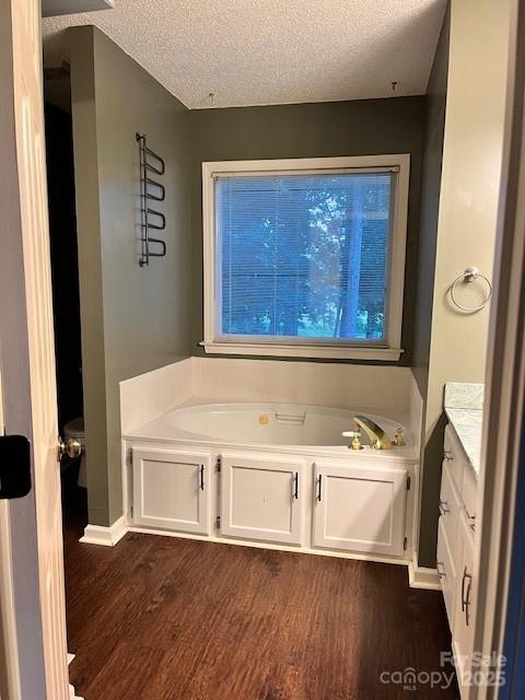 bathroom with a textured ceiling, a garden tub, wood finished floors, vanity, and baseboards