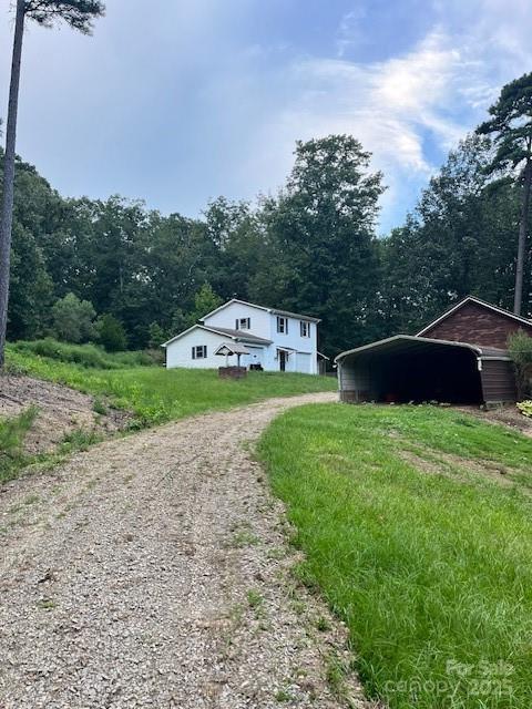 view of side of home with driveway, a carport, a forest view, and a lawn