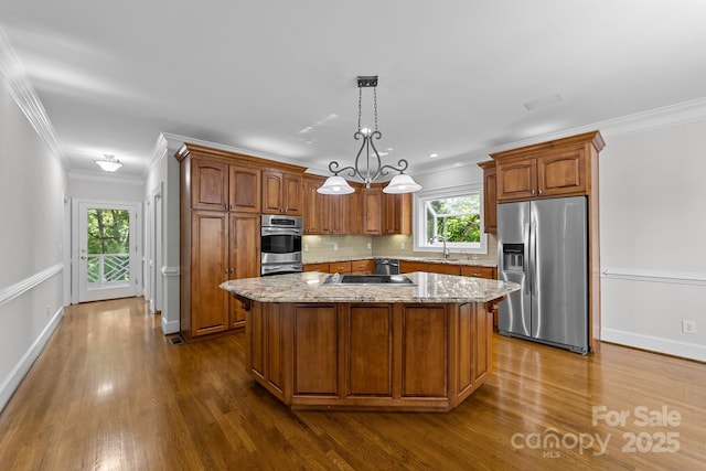 kitchen with appliances with stainless steel finishes, hanging light fixtures, light stone countertops, a kitchen island, and crown molding