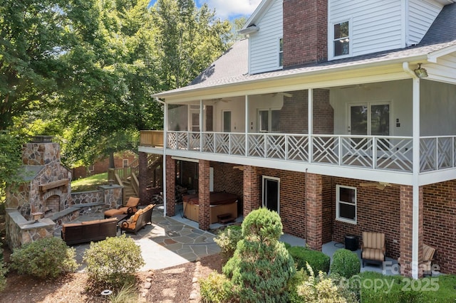 rear view of house with brick siding, a patio, a shingled roof, a hot tub, and an outdoor living space with a fireplace