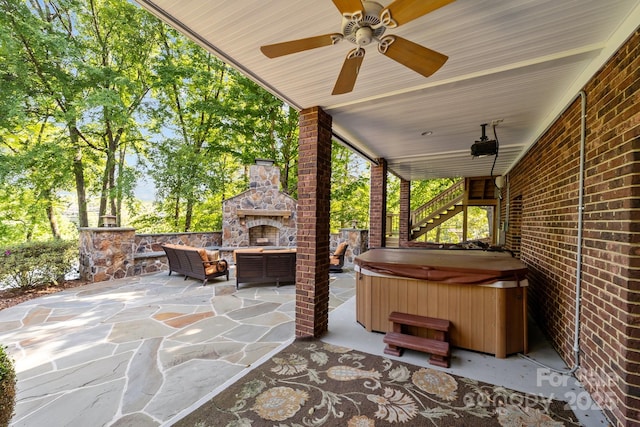 view of patio with ceiling fan, an outdoor living space with a fireplace, and a hot tub