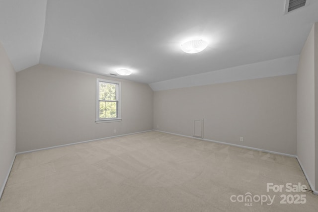 additional living space with lofted ceiling, baseboards, visible vents, and light colored carpet