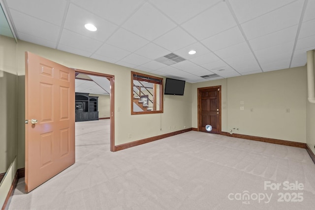 basement with light carpet, visible vents, a paneled ceiling, and baseboards