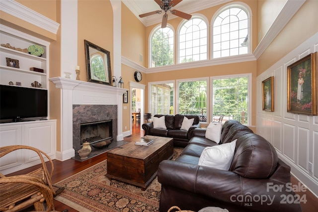 living room with hardwood / wood-style floors, ceiling fan, a high end fireplace, crown molding, and built in shelves