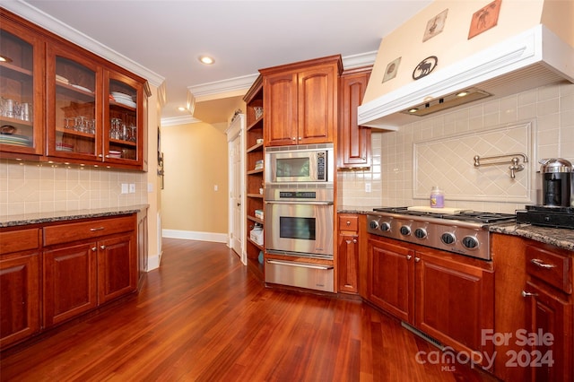 kitchen with ventilation hood, appliances with stainless steel finishes, dark hardwood / wood-style flooring, and dark stone counters