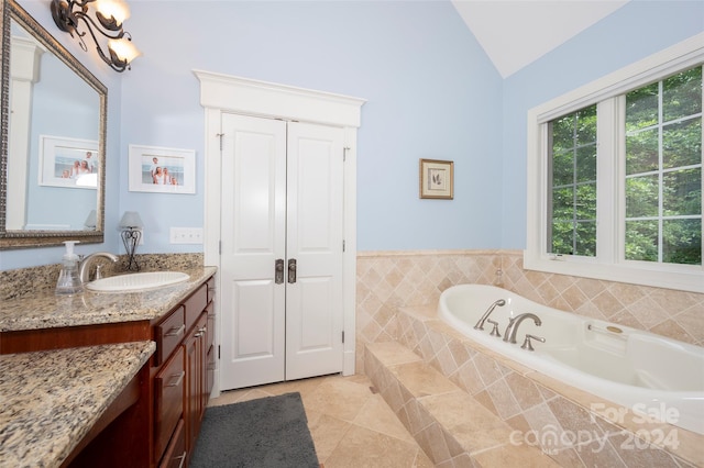 bathroom with a relaxing tiled tub, tile patterned floors, lofted ceiling, and vanity