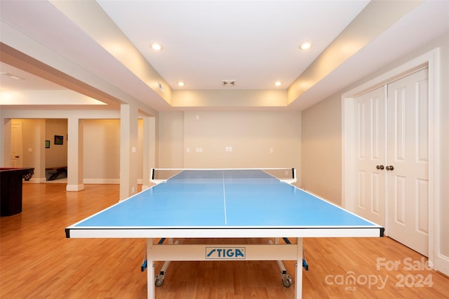 recreation room with wood-type flooring and a tray ceiling