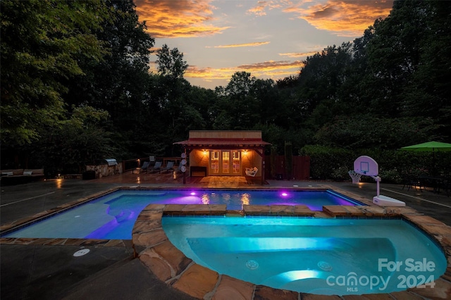 pool at dusk with an outdoor structure and a patio area