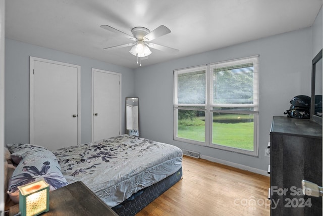 bedroom featuring ceiling fan, two closets, multiple windows, and light hardwood / wood-style floors