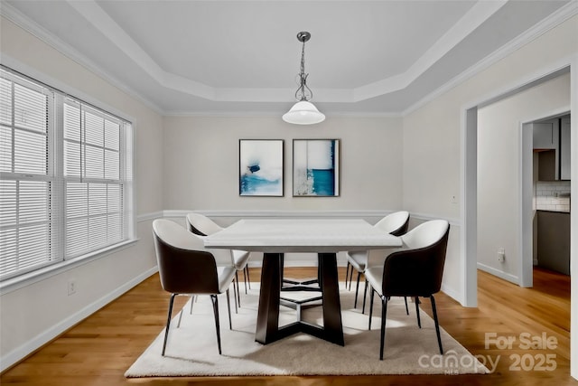 dining space with crown molding, a tray ceiling, and light hardwood / wood-style flooring