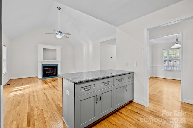 kitchen featuring light stone counters, lofted ceiling, light hardwood / wood-style flooring, and gray cabinetry