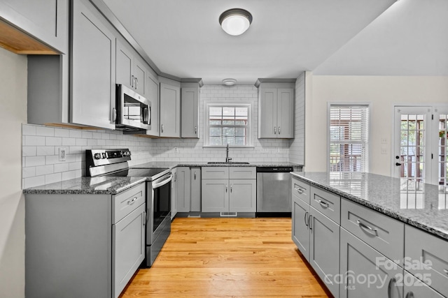 kitchen with sink, stone countertops, light hardwood / wood-style flooring, gray cabinets, and stainless steel appliances