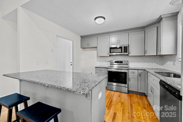 kitchen with sink, a kitchen bar, light stone countertops, and appliances with stainless steel finishes