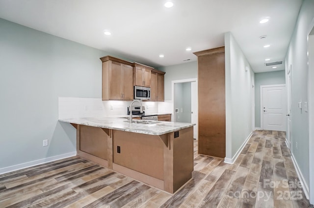 kitchen featuring kitchen peninsula, sink, light hardwood / wood-style floors, decorative backsplash, and stainless steel appliances