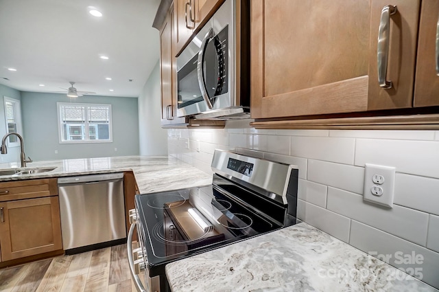 kitchen featuring light hardwood / wood-style floors, appliances with stainless steel finishes, decorative backsplash, sink, and light stone counters