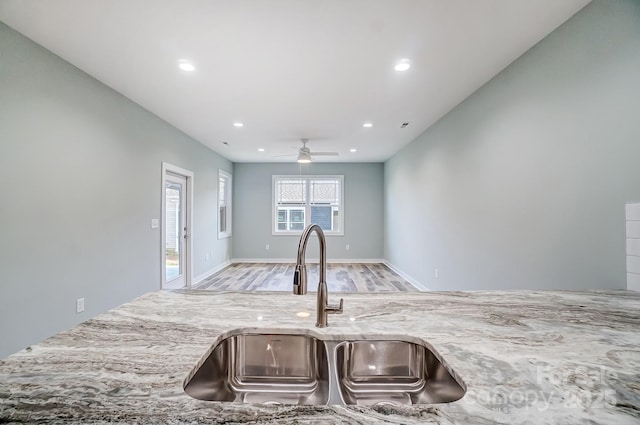 kitchen with sink, light wood-type flooring, ceiling fan, and light stone countertops