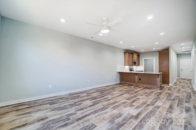 unfurnished living room featuring ceiling fan, sink, and light wood-type flooring