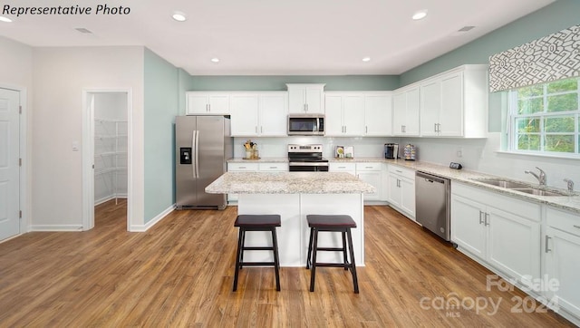 kitchen with a kitchen island, appliances with stainless steel finishes, white cabinetry, sink, and light stone counters