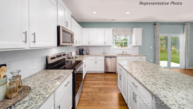 kitchen featuring sink, light stone counters, light wood-type flooring, stainless steel appliances, and white cabinets