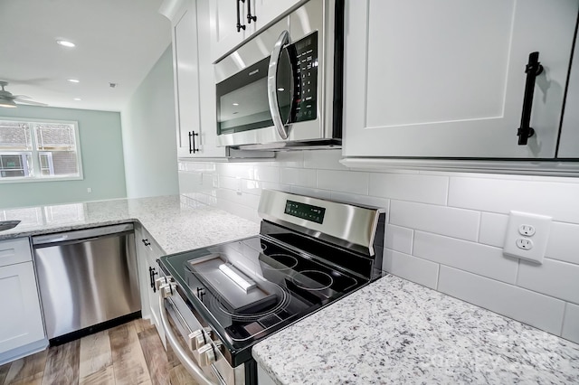 kitchen with white cabinets, appliances with stainless steel finishes, backsplash, light stone counters, and light hardwood / wood-style flooring