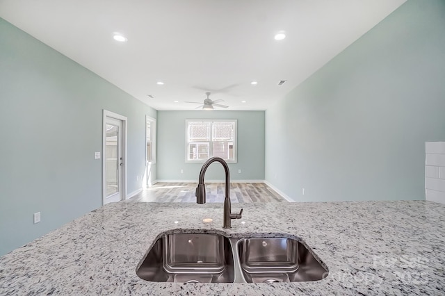 kitchen featuring light stone countertops, sink, ceiling fan, and light wood-type flooring