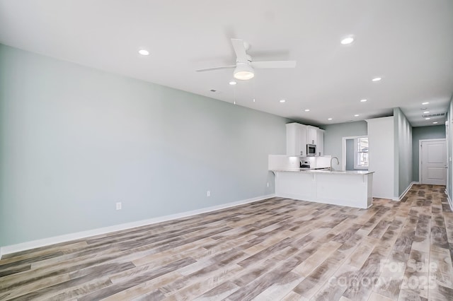 unfurnished living room with ceiling fan, sink, and light hardwood / wood-style flooring