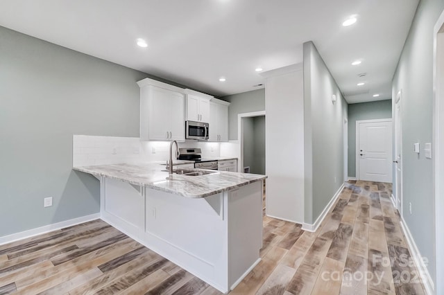 kitchen featuring appliances with stainless steel finishes, white cabinetry, kitchen peninsula, light hardwood / wood-style flooring, and a breakfast bar area