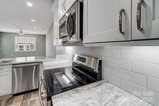 kitchen featuring light stone countertops, white cabinets, stainless steel appliances, light hardwood / wood-style floors, and backsplash