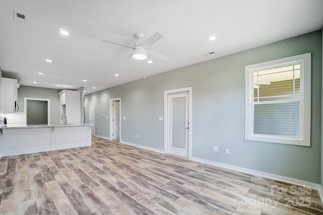 unfurnished living room with sink, light hardwood / wood-style floors, and ceiling fan