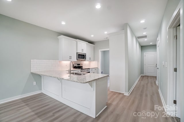 kitchen with kitchen peninsula, backsplash, white cabinetry, and appliances with stainless steel finishes