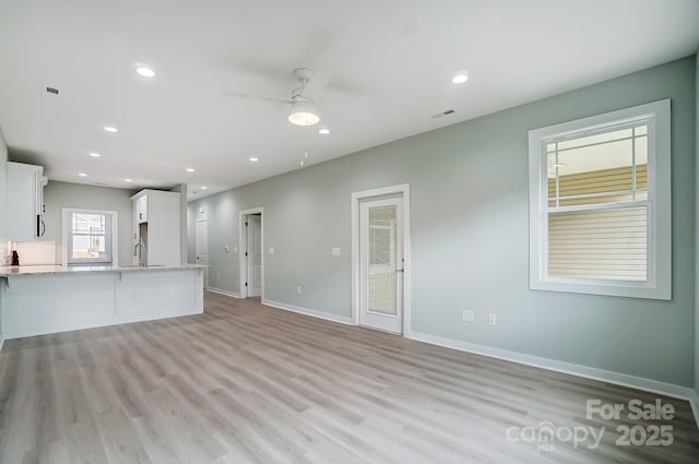 unfurnished living room with ceiling fan, sink, and light wood-type flooring