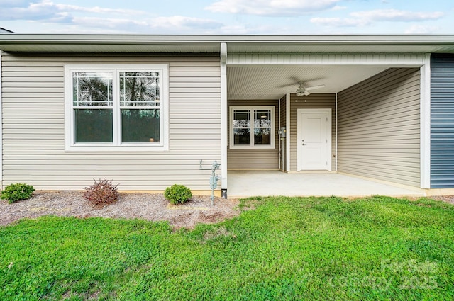 entrance to property with a patio area, a yard, and ceiling fan