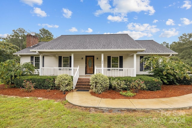 view of front of house with a shingled roof, a chimney, a porch, and a front yard